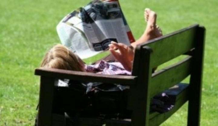 Muž ležící na lavičce a držící noviny