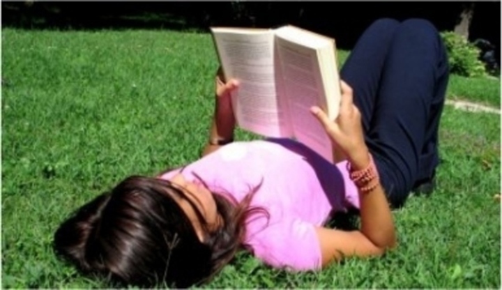 Dívka ležící na trávě drží v rukách knihu 