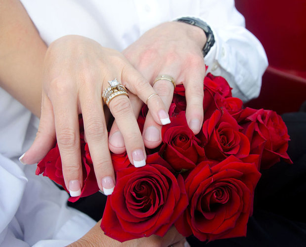 Ruce se snubními prstýnky položené na kytici rudých růží