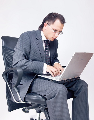 Muž sedící na kancelářském křesle s počítačem na kolenou